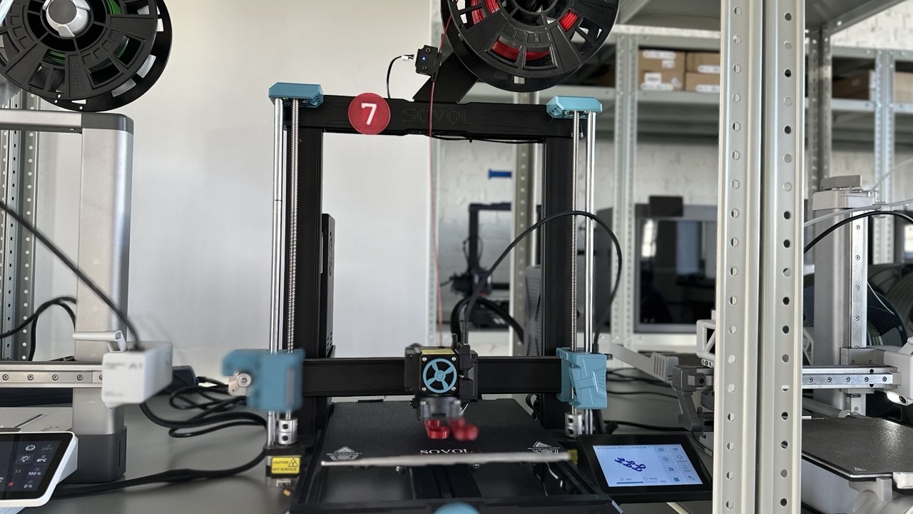 ATRIMUT 设备区架子上的 Sovol SV06 ACE FDM 3D打印机，顶部装有耗材卷